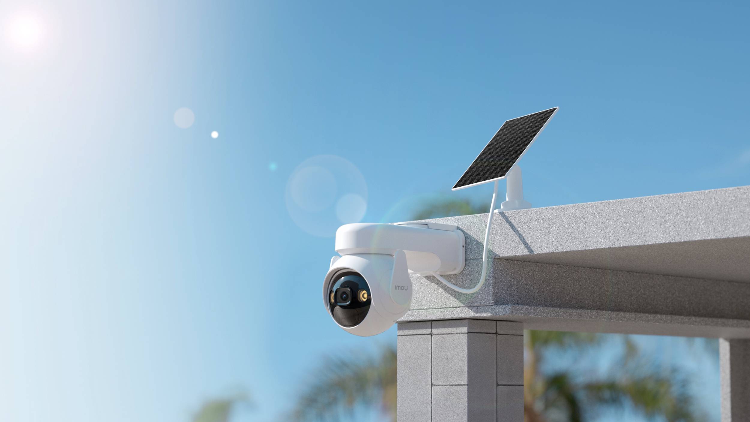'Eine weiße Überwachungskamera mit Solarpanel ist an einer Gebäudeecke im Freien montiert. Der Himmel ist klar und sonnig.'