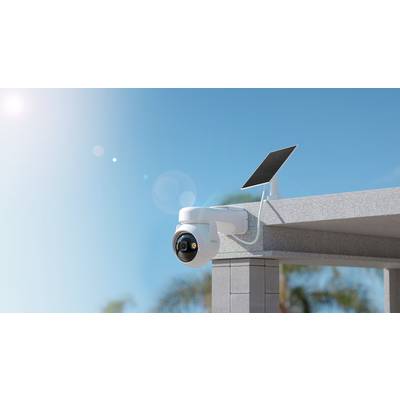 'Eine weiße Überwachungskamera mit Solarpanel ist an einer Gebäudeecke im Freien montiert. Der Himmel ist klar und sonnig.'