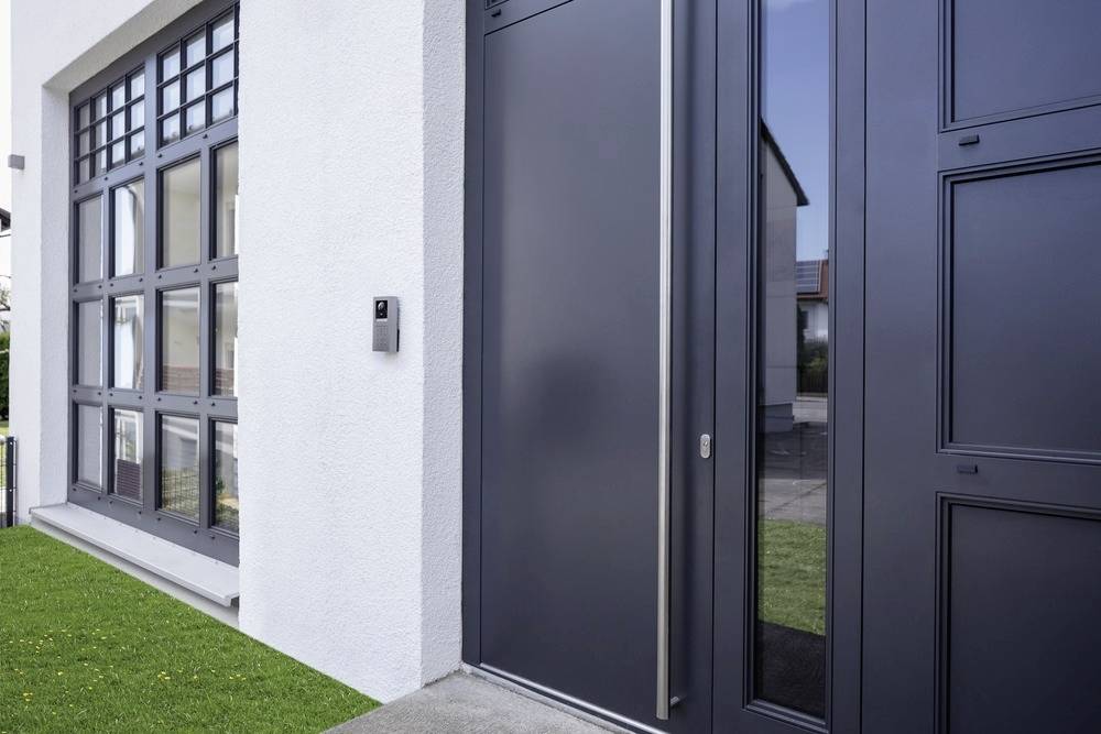 Eingangsbereich eines modernen Hauses mit großer, dunkler Tür und Fensterfront.