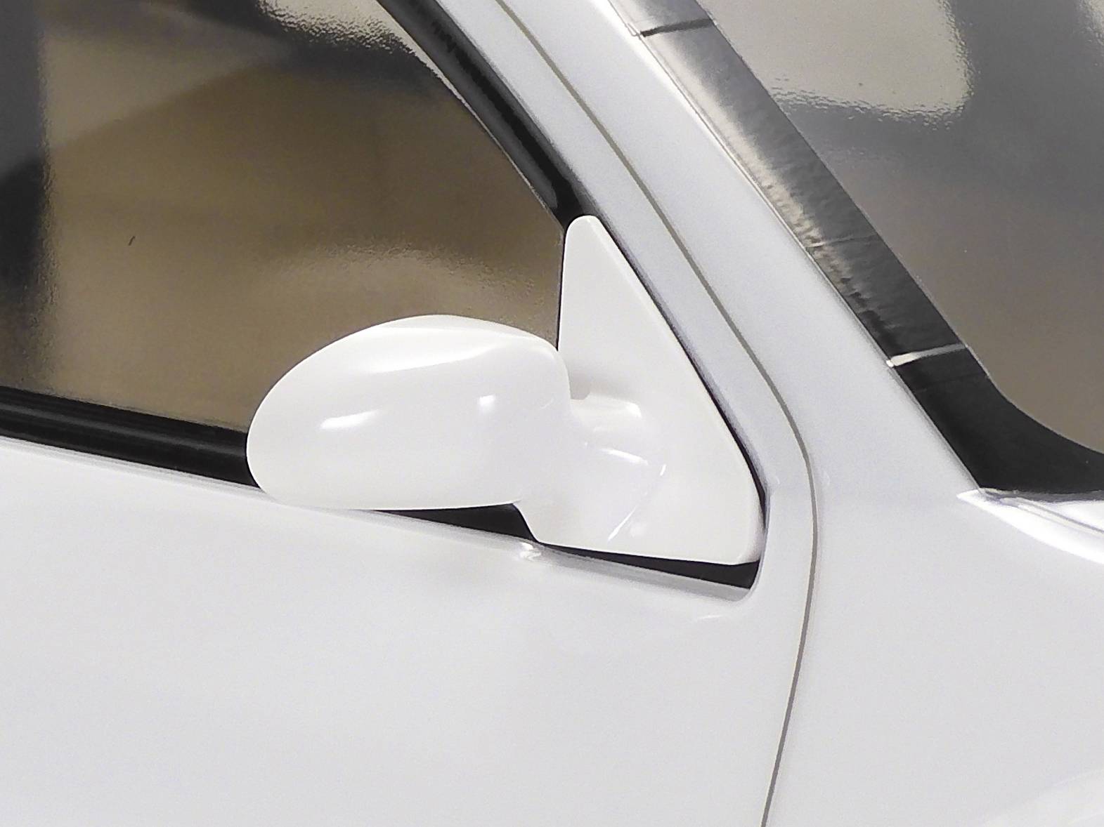 Nahaufnahme eines weißen Seitenspiegels an einem Auto, das den Fokus auf das geschwungene Design und die glänzende Oberfläche legt.