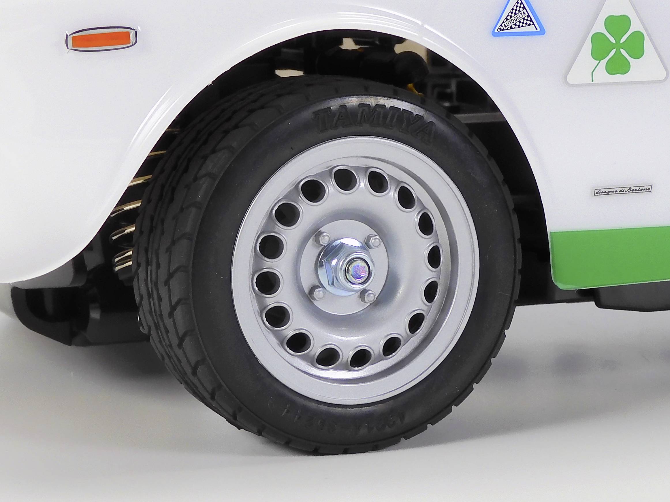 Nahaufnahme eines weißen Autos mit Aluminiumfelge und schwarzem Reifen. Ein grünes Kleeblatt-Logo ist auf dem Kotflügel abgebildet.