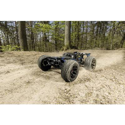Ferngesteuertes Auto fährt schnell auf einem sandigen Waldweg. Die großen Reifen wirbeln Staub auf. Hintergründe sind Bäume.