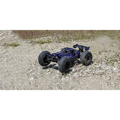 Ein ferngesteuertes Auto fährt auf einem steinigen Gelände, aufgewirbelter Staub zeigt Bewegung an. Grasbewuchs im Hintergrund.
