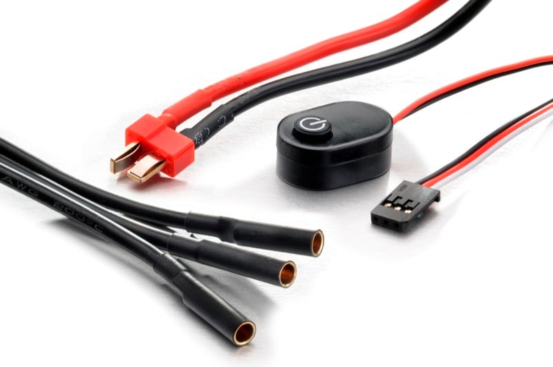 Verschiedene Kabelstränge mit einem Ein/Aus-Schalter. Links befinden sich schwarze Kabel mit Steckverbindungen; rechts rote und schwarze Kabel.
