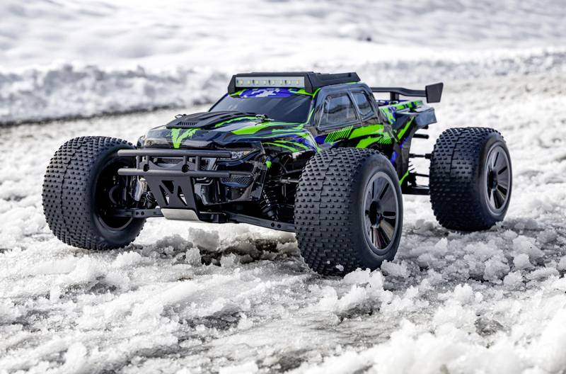 Ein ferngesteuertes Auto mit grünem und schwarzem Muster fährt im Schnee. Es hat große Reifen, die für unebene, schneebedeckte Flächen geeignet sind.
