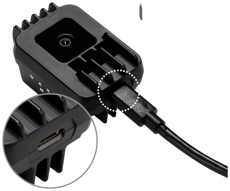 Ein schwarzes Elektronikgerät ist mit einem Ladekabel verbunden. Im vergrößerten Kreis sieht man den Anschluss für das Kabel.