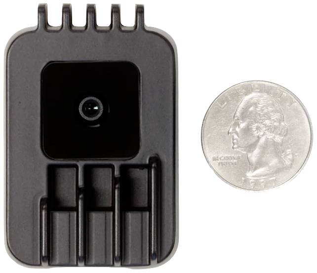 Ein kleines elektronisches Gerät neben einer Münze zum Größenvergleich. Das Gerät hat eine Kamera, die nach vorne zeigt.