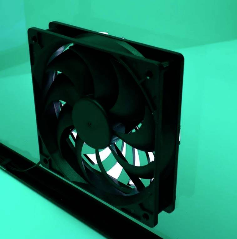 'Ein schwarzer Computerlüfter ist an einer grünen Wand montiert. Das Bild zeigt den Lüfter in einer schrägen Nahaufnahme.'