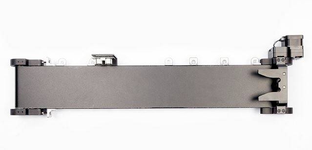 Langes schwarzes Metallteil mit seitlichen Halterungen und einem elektromagnetischen Bauteil an einem Ende, auf weißem Hintergrund.