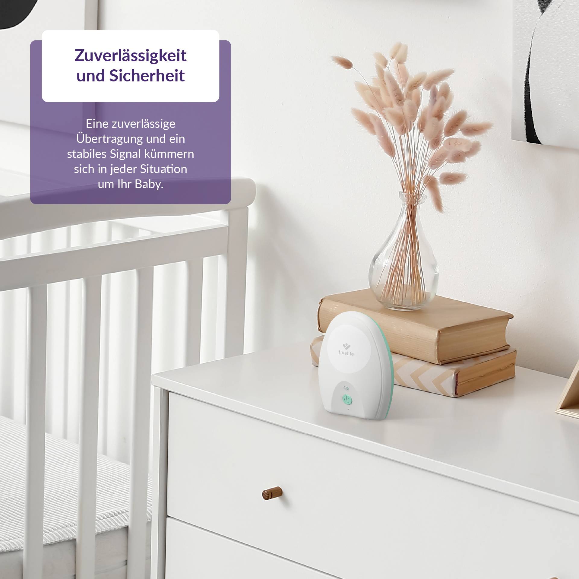 Ein Babyzimmer mit einem weißen Babyphone auf einer Kommode, daneben zwei Bücher und eine Vase mit getrockneten Gräsern.