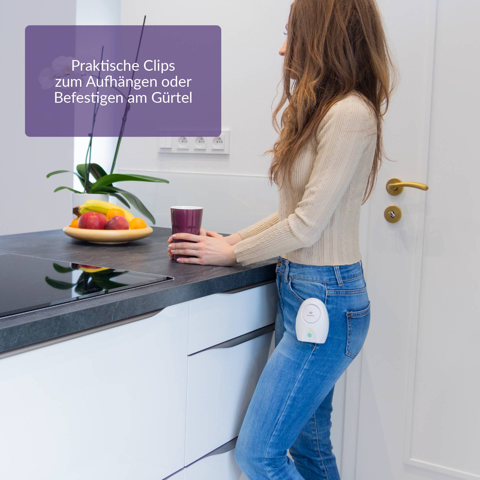 Frau steht in einer modernen Küche, hält eine Tasse, trägt ein tragbares Gerät am Gürtel. Text: 'Praktische Clips zum Aufhängen oder Befestigen am Gürtel'.