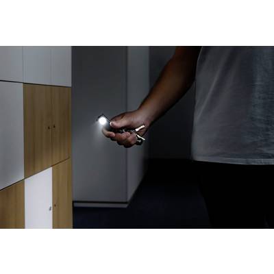 Eine Person beleuchtet mit einem Taschenlampenschlüsselanhänger einen dunklen Flur neben einem Schrank.