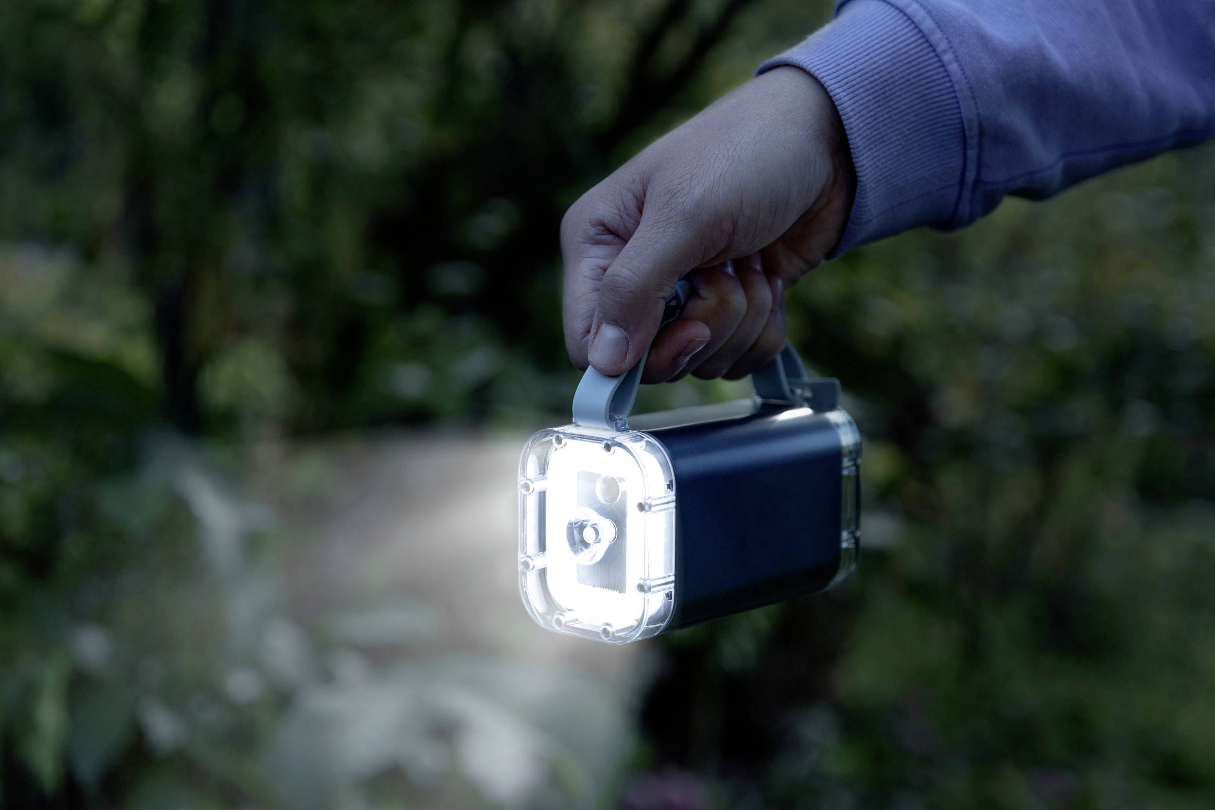 Eine Person hält eine leuchtende Taschenlampe im Freien, die Licht auf den Boden strahlt.