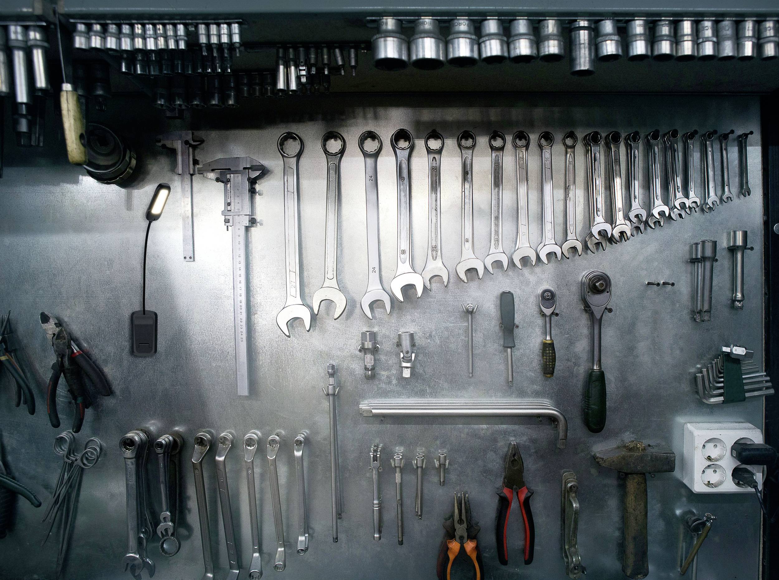 Ein ordentlich angeordneter Werkzeugsatz an einer Metallwand, darunter Schraubenschlüssel, Hammer, Zangen und ein Messschieber.