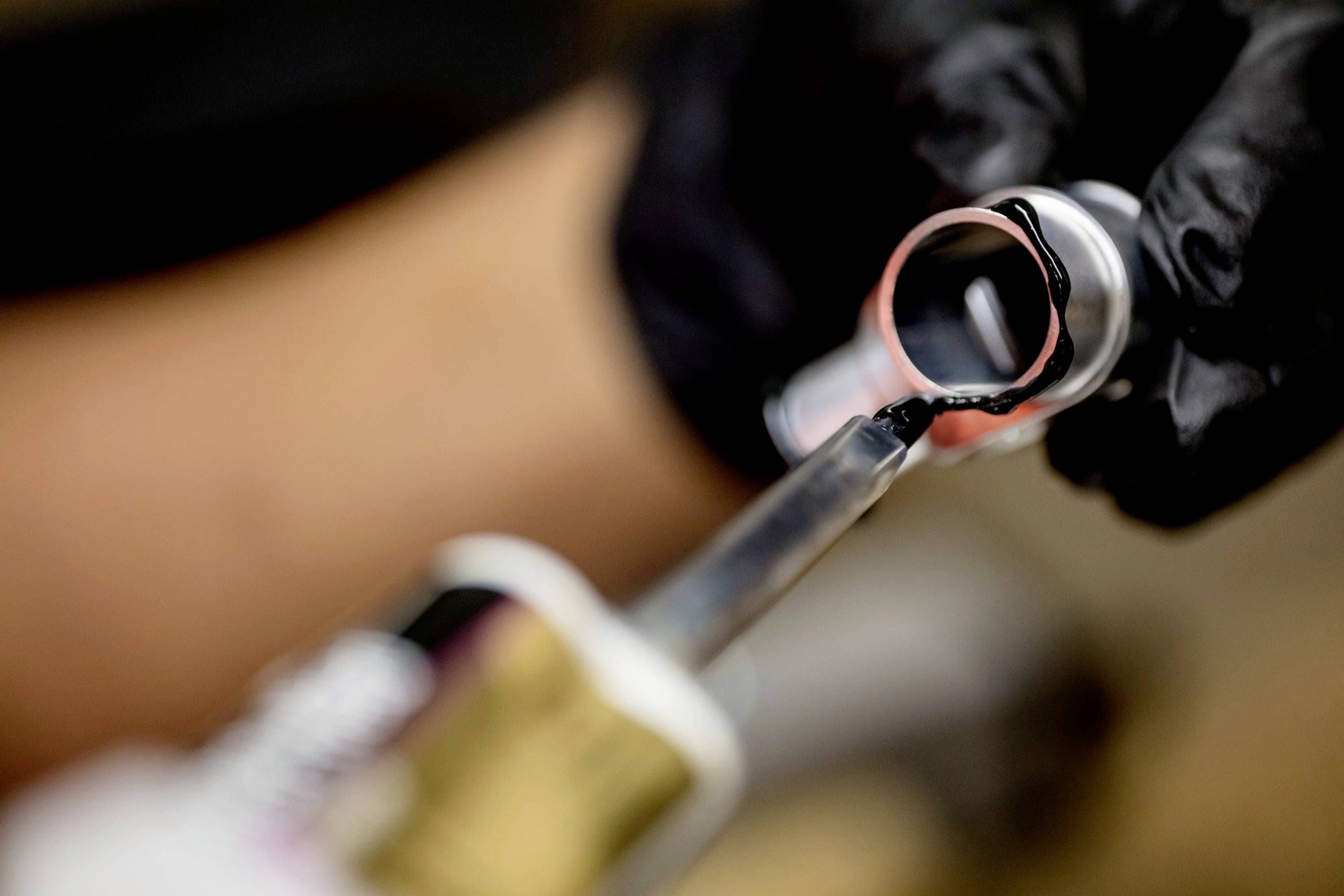 Nahaufnahme von Händen in schwarzen Handschuhen, die eine Klebepistole benutzen, um einen schwarzen Kleber auf ein Metallrohr aufzutragen.