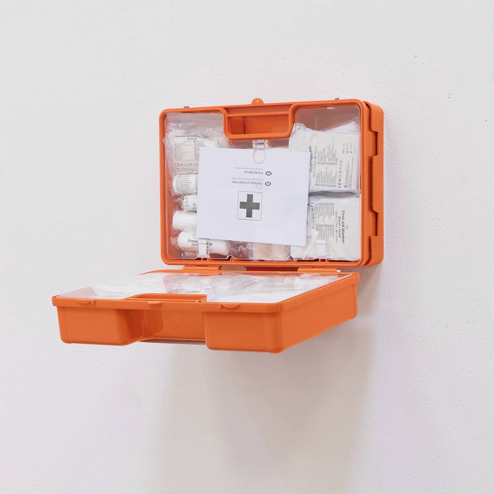 Offener Erste-Hilfe-Kasten an einer weißen Wand, gefüllt mit Verbandsmaterial, Pflastern und medizinischen Anweisungen.