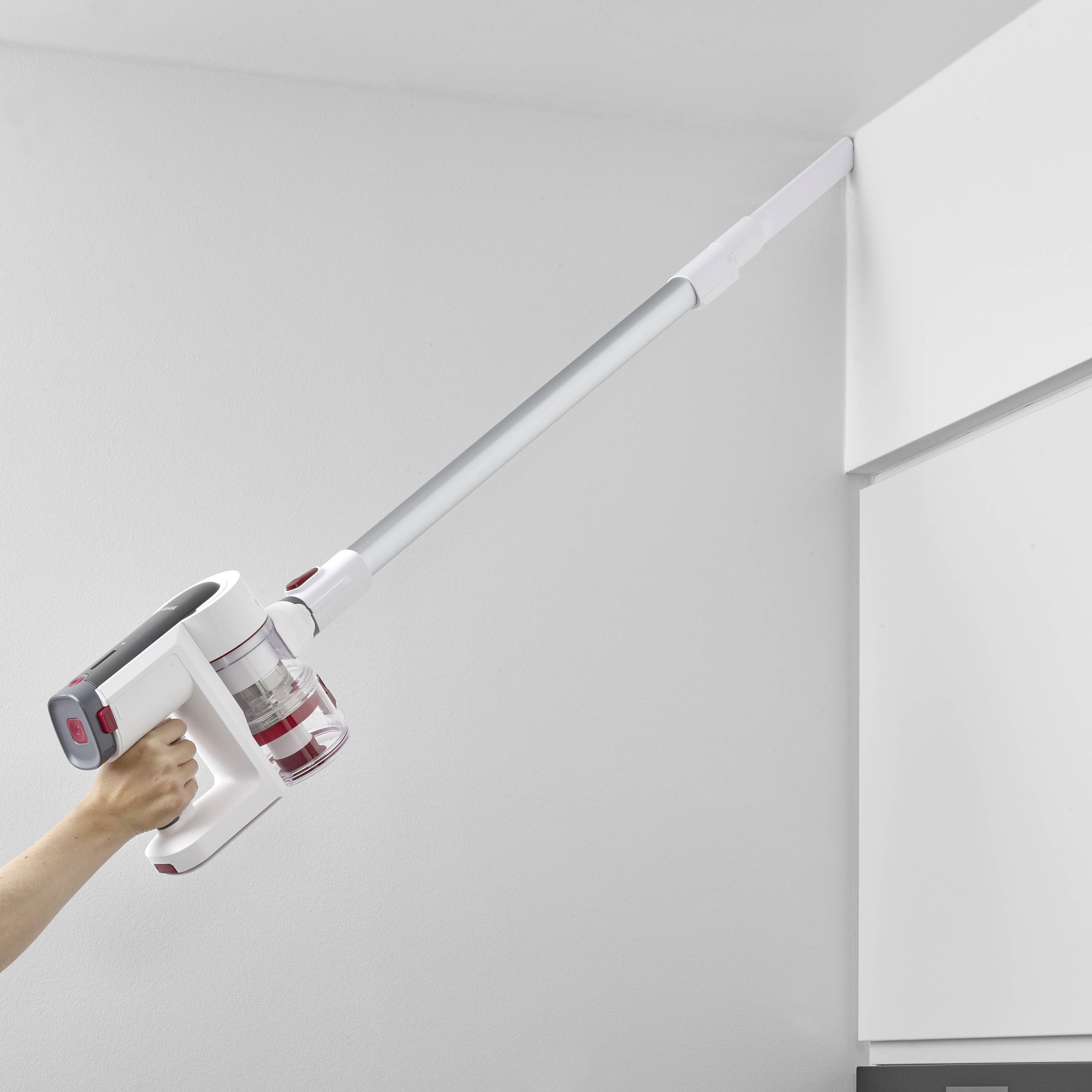 Eine Person verwendet einen kabellosen Staubsauger mit langem Rohr, um eine Ecke an der Decke zu reinigen.