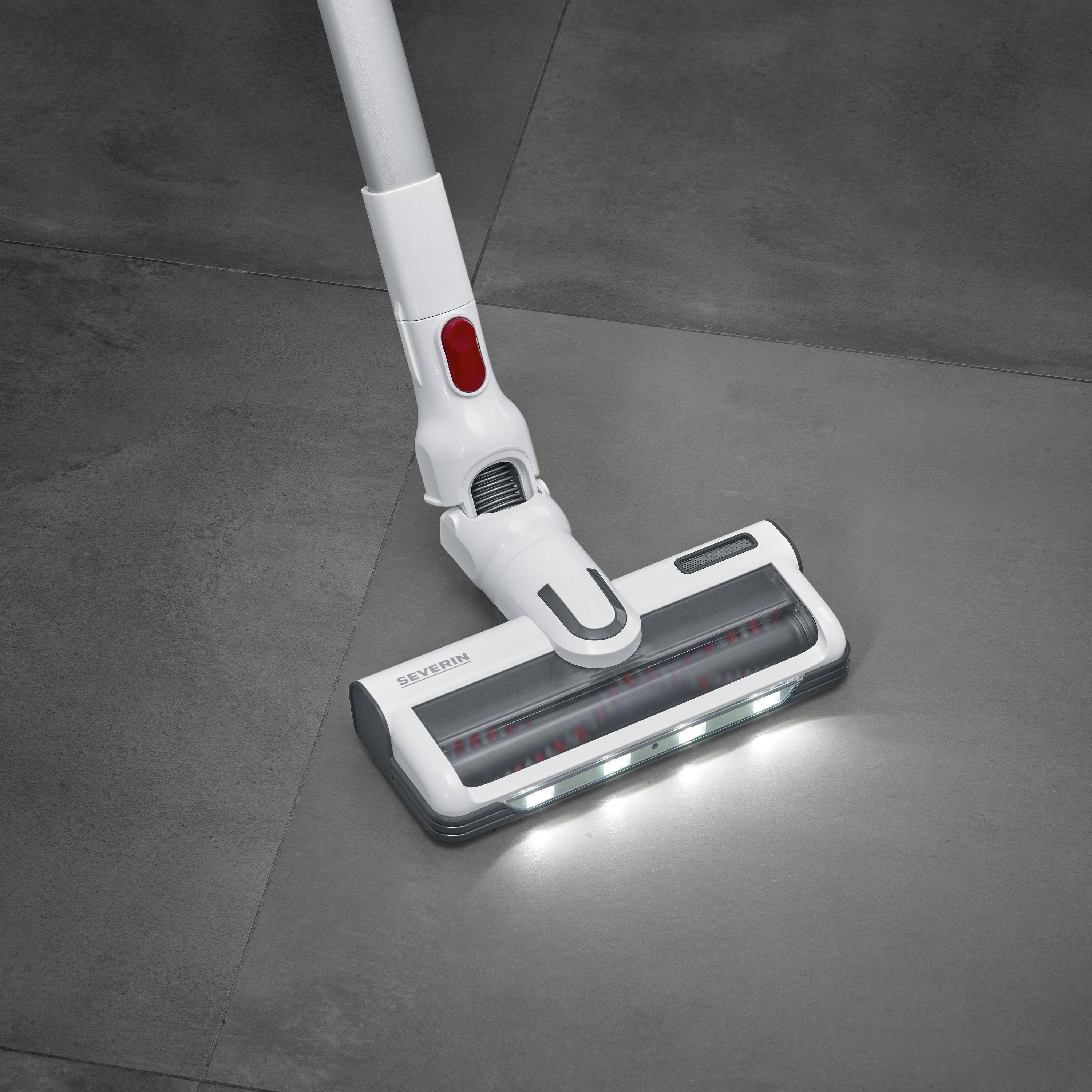 Ein weißer Staubsaugerkopf mit LED-Lichtern, der über einen dunklen Fliesenboden gleitet.