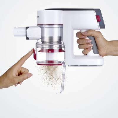 Eine Hand hält einen Staubsauger, während eine andere Hand auf einen teilentleerten Staubbehälter zeigt. Staub fällt heraus.