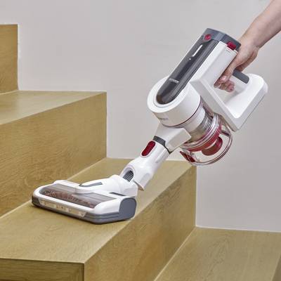 Eine Person reinigt Treppenstufen mit einem kabellosen, handgehaltenen Staubsauger auf Holztreppe. Focus auf Effizienz und Ergonomie.