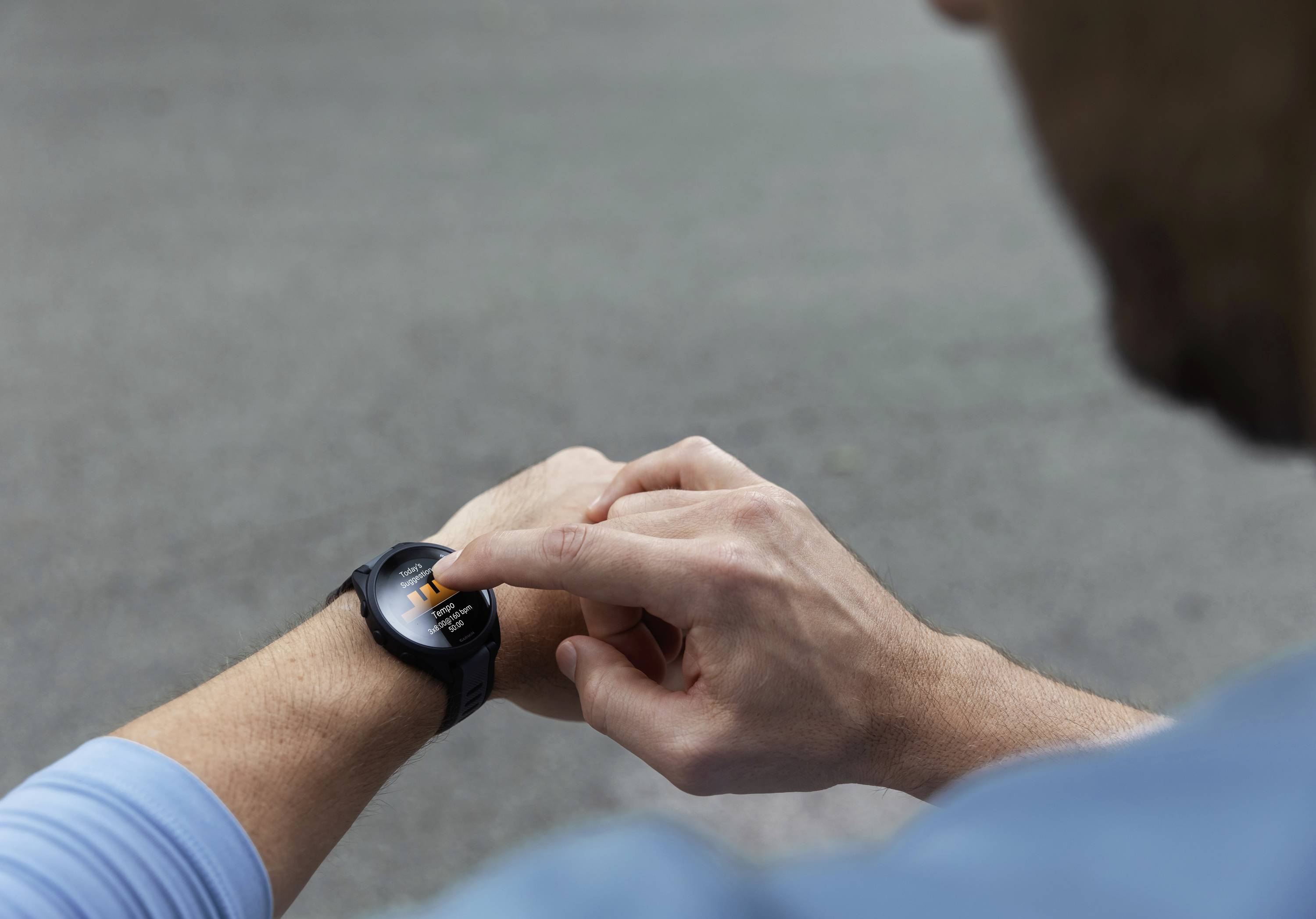 Eine Person benutzt eine Smartwatch, tippt auf den Bildschirm im Freien. Sie trägt ein hellblaues Oberteil, Fokus auf Technologie-Nutzung.