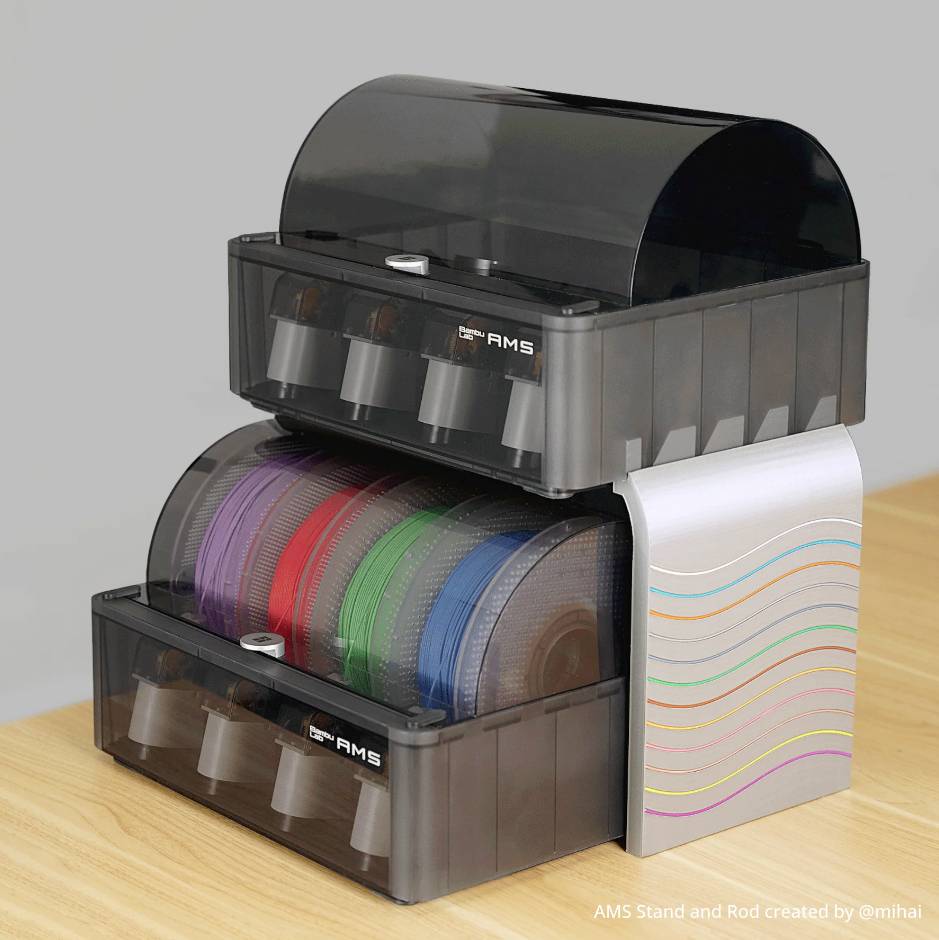 'Zwei schwarze Filamenthalter mit Rollen in verschiedenen Farben, übereinander gestapelt auf einem Holztisch.'