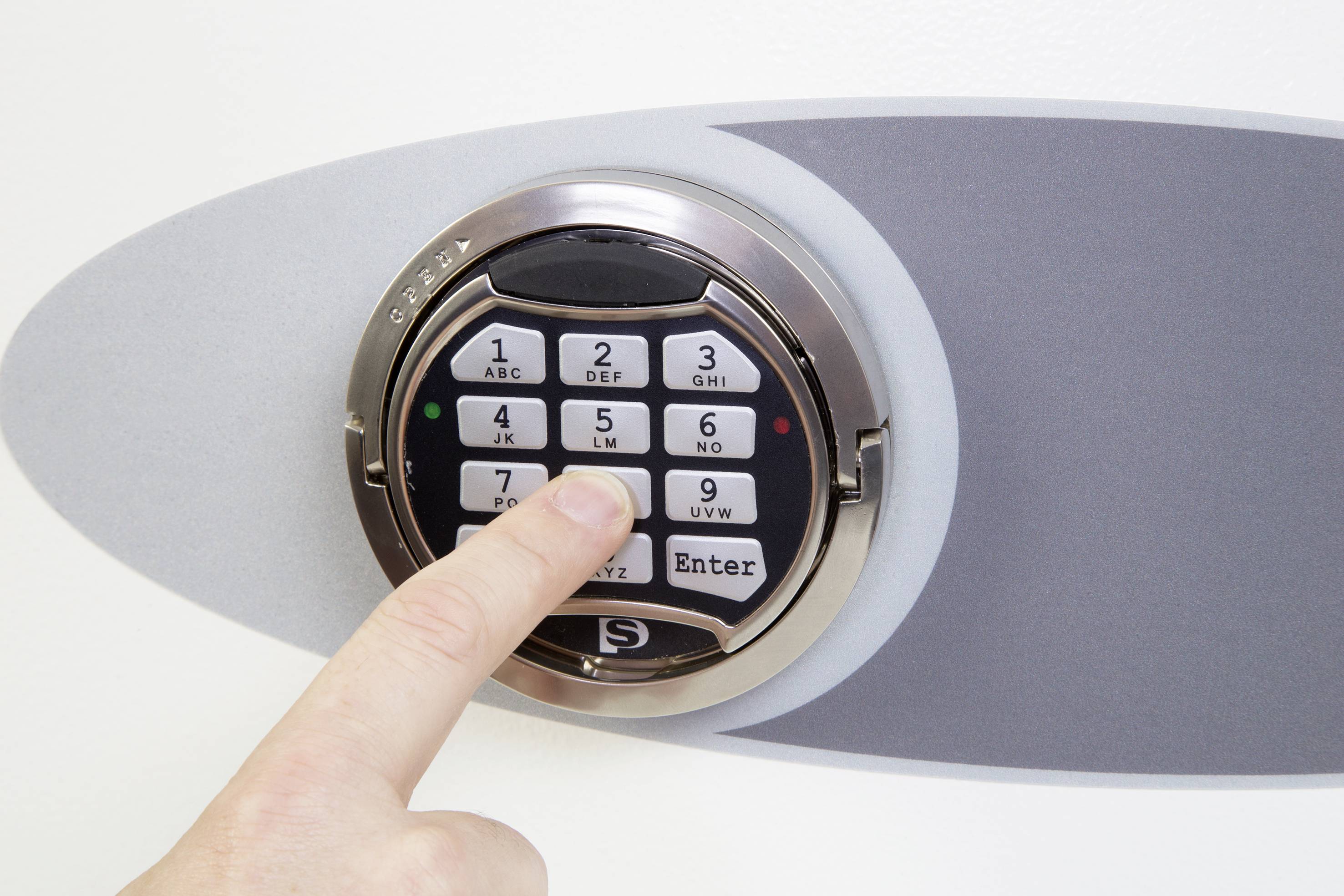 Eine Hand drückt eine Taste auf einem elektronischen Zahlenschloss, das an einem Safe angebracht ist.
