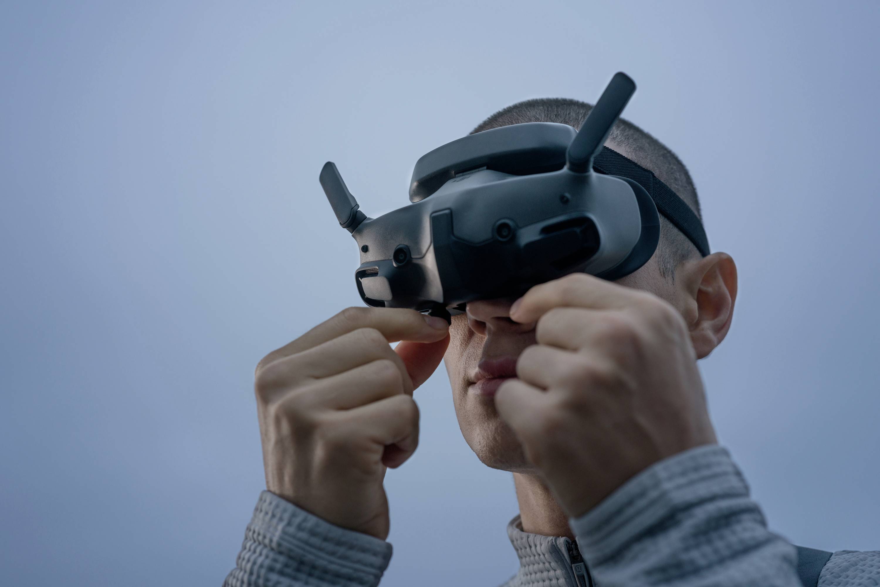 Eine Person trägt eine VR-Brille und hält sie fest. Der Hintergrund ist blau und wolkenlos.