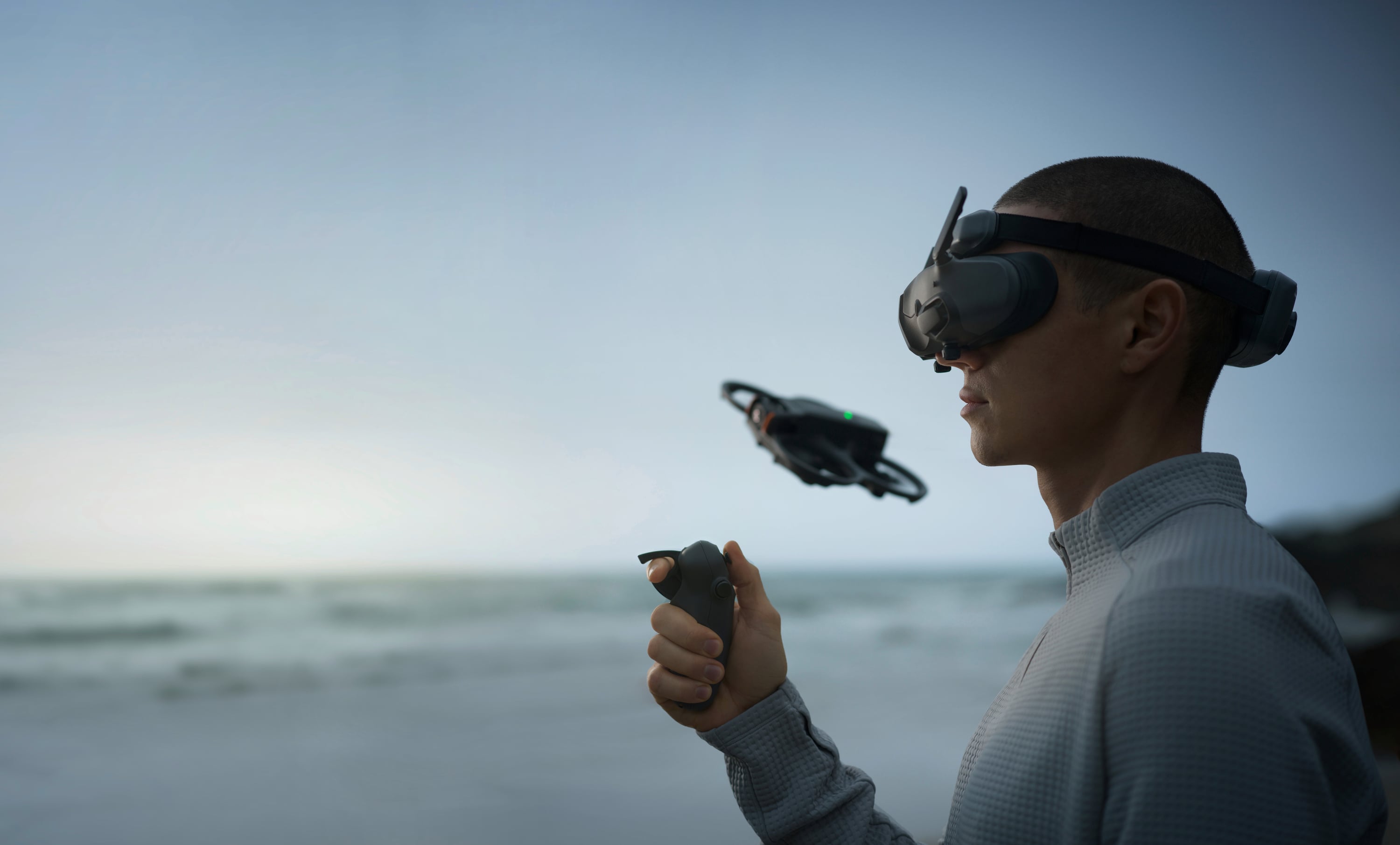 Person mit VR-Brille steuert eine Drohne am Strand mit einem Controller. Ozeanhorizont im Hintergrund.