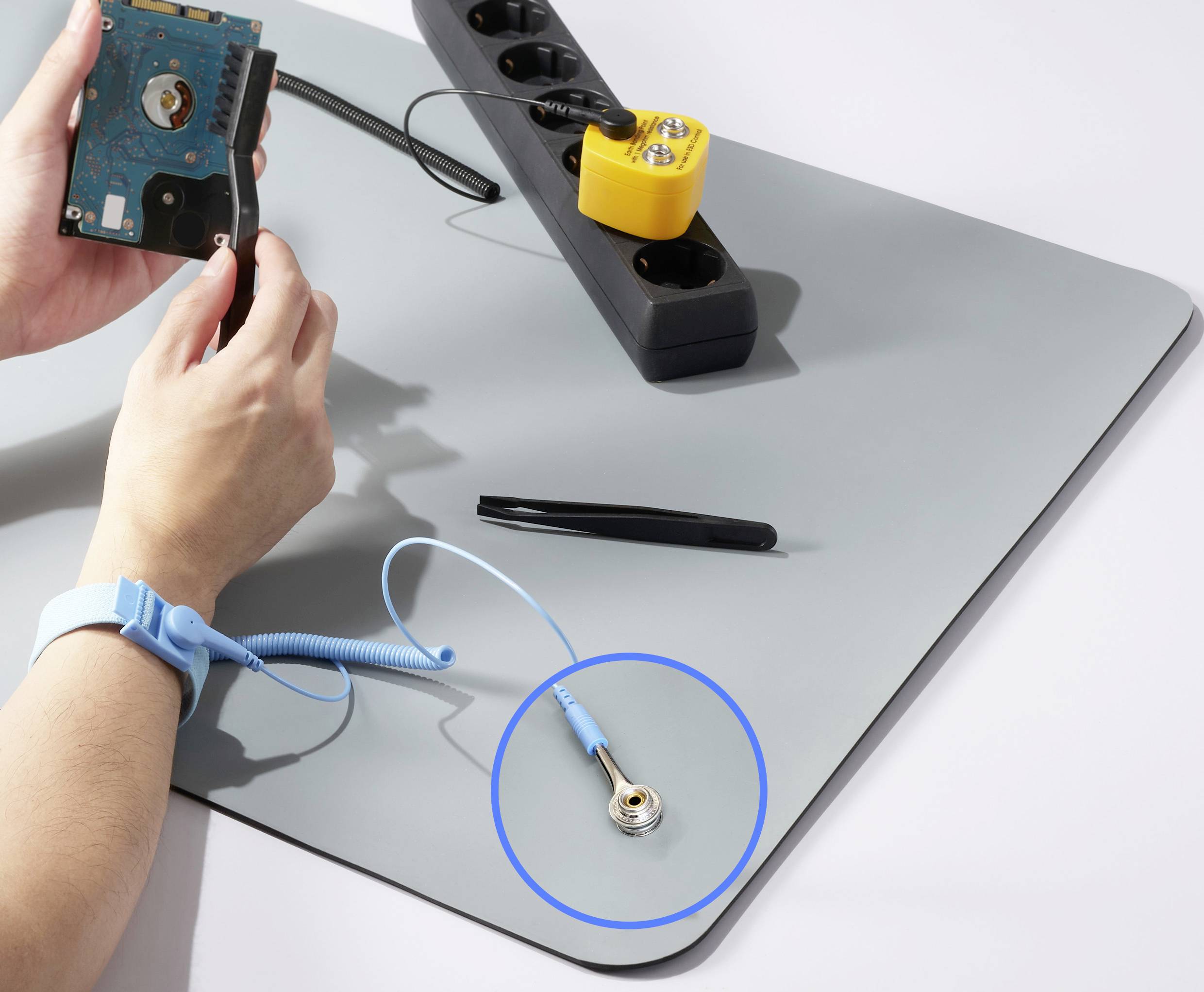 Eine Person arbeitet mit einer Festplatte und einem Armband für antistatische Entladung auf einer grauen Matte. Im Hintergrund eine Steckdosenleiste.