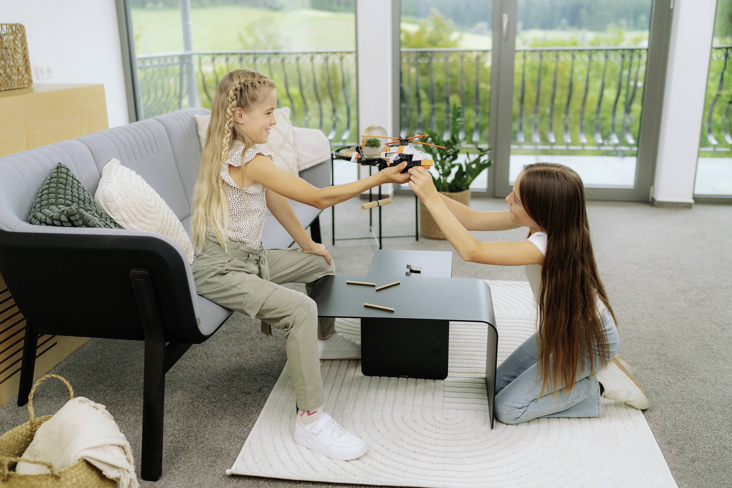 Zwei Mädchen sitzen in einem Wohnzimmer und spielen fröhlich ein Videospiel auf einer Konsole, umgeben von moderner Einrichtung.