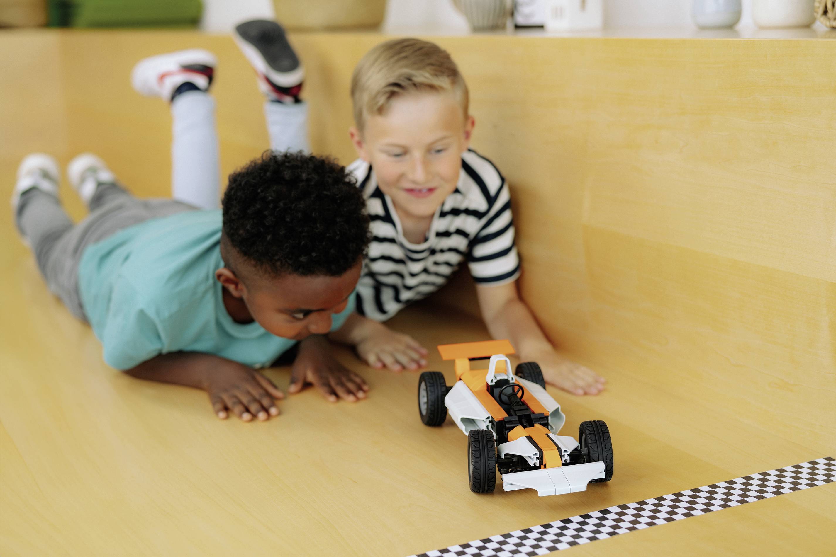 Zwei Jungen beobachten aufmerksam ein kleines Spielzeugauto, das auf einer Holzoberfläche auf eine Ziellinie zusteuert.