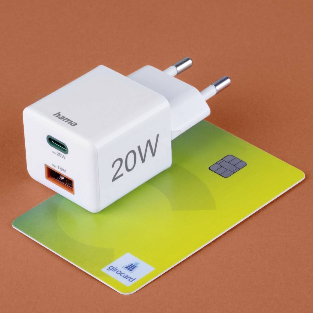 'Ladegerät mit 20W-Anzeige und USB-Anschlüssen, auf einer grünen girocard platziert, vor braunem Hintergrund.'