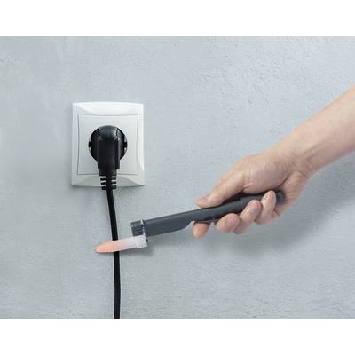 Eine Hand testet mit einem Prüfgerät die Spannung an einer Steckdose, in die ein schwarzer Stecker eingesteckt ist.