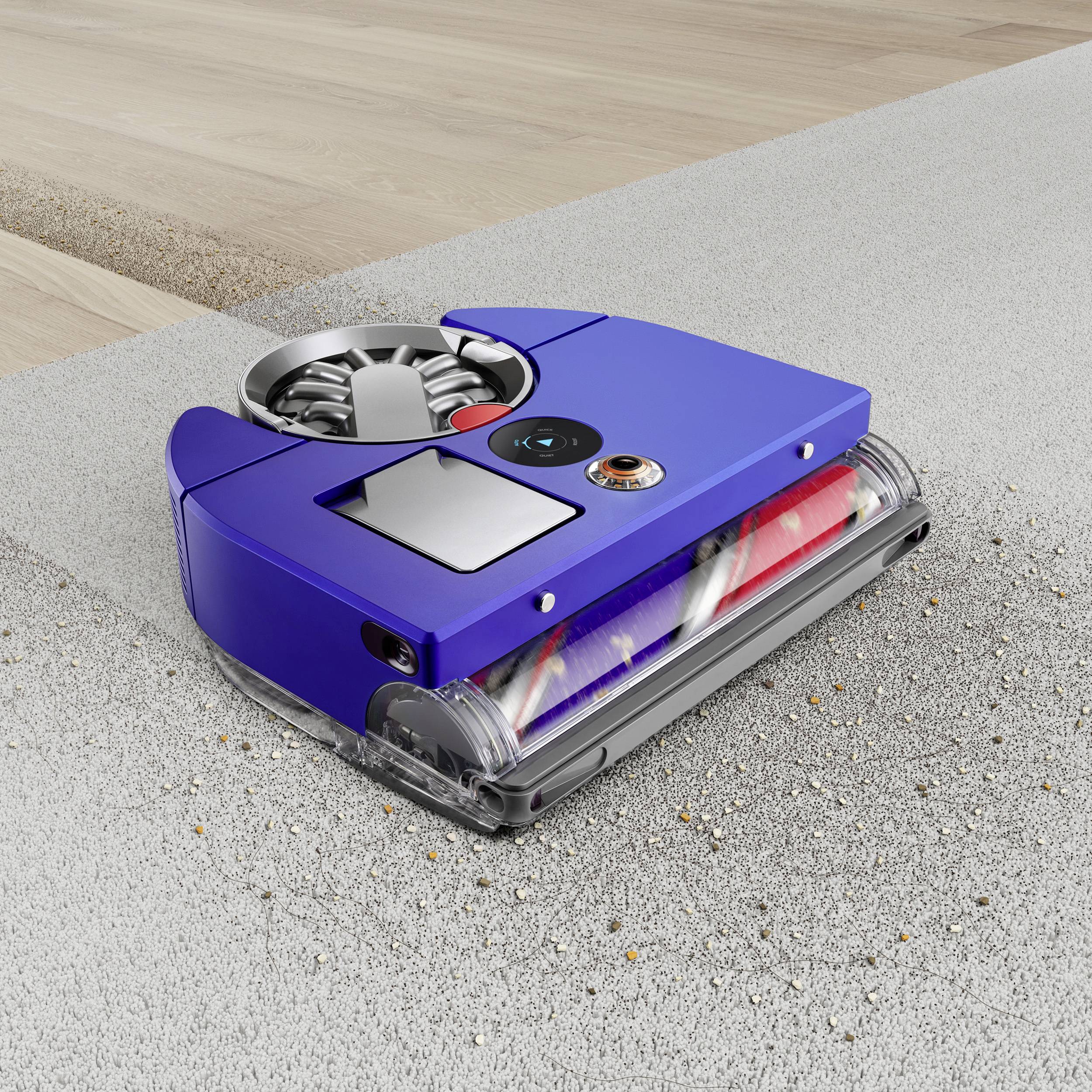 Ein blauer Roboter-Staubsauger reinigt einen Teppich an der Nahtstelle zum Parkettboden. Er saugt Schmutz und Staub effektiv auf.