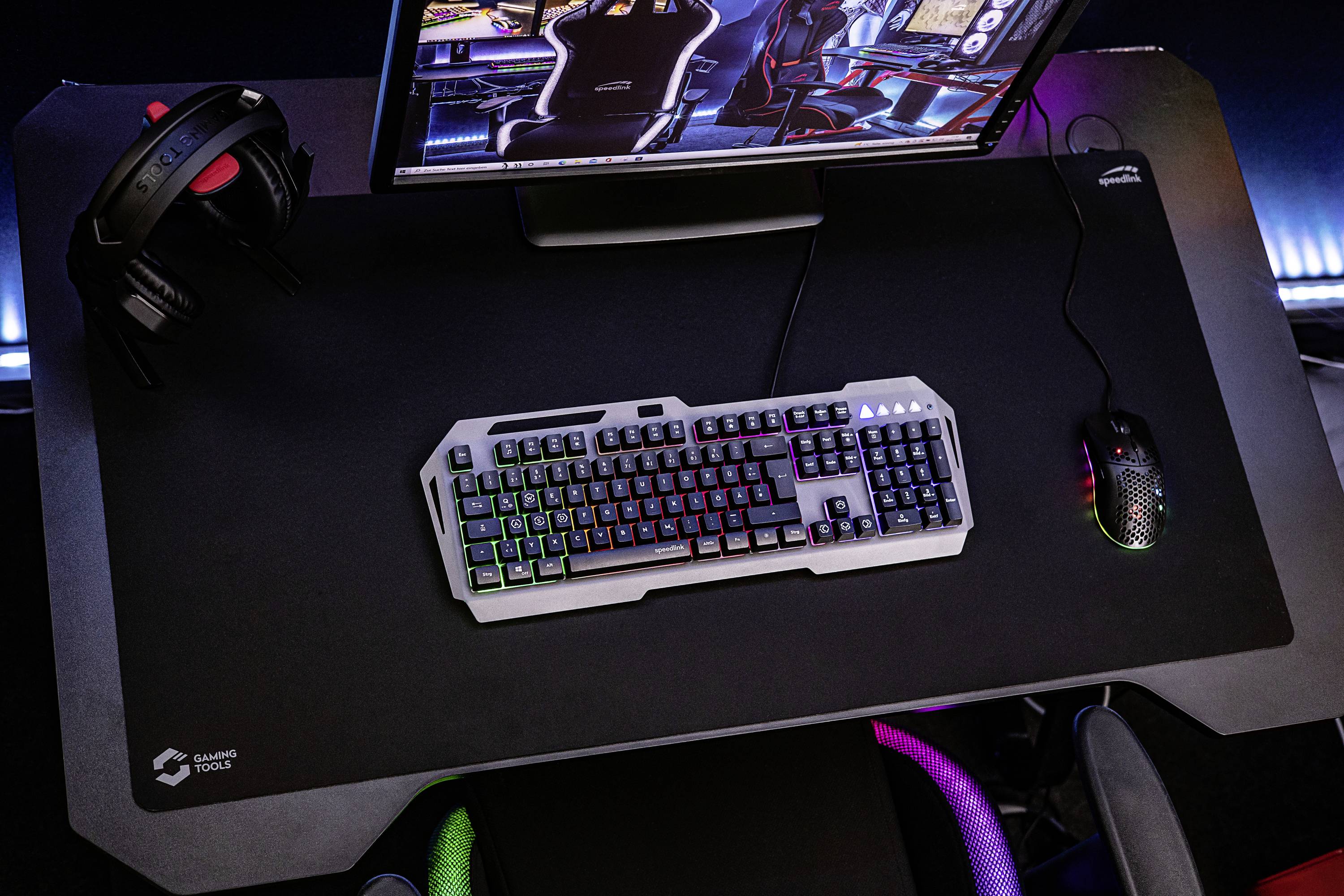 Gaming-Setup mit Tastatur, Maus und Kopfhörer auf einem großen Mauspad. Ein Bildschirm zeigt ein Spielmenü.