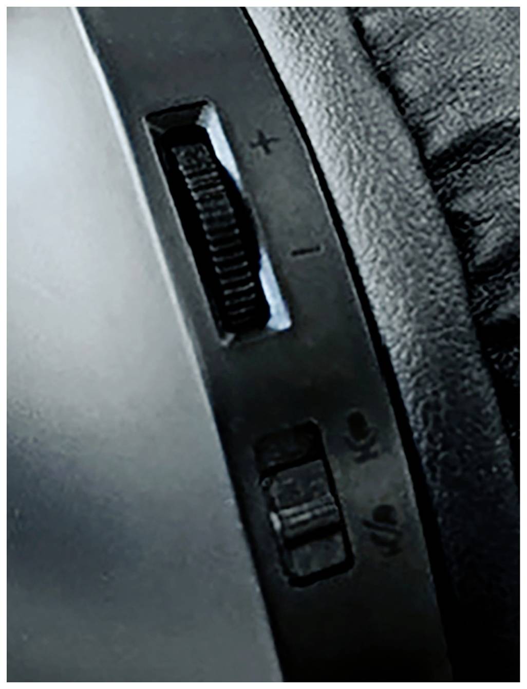 Nahaufnahme eines Lautstärkereglers und Schalters auf einem Kopfhörer. Der Regler hat Plus- und Minus-Symbole; der Schalter zeigt Mikrofon an/aus.