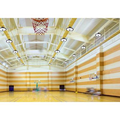 Eine leere Sporthalle mit Holzboden und Basketballkörben an den Seiten. Die Decke ist hoch mit sichtbaren Trägern und Lichtern.