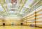 Eine leere Sporthalle mit Holzboden und Basketballkörben an den Seiten. Die Decke ist hoch mit sichtbaren Trägern und Lichtern.