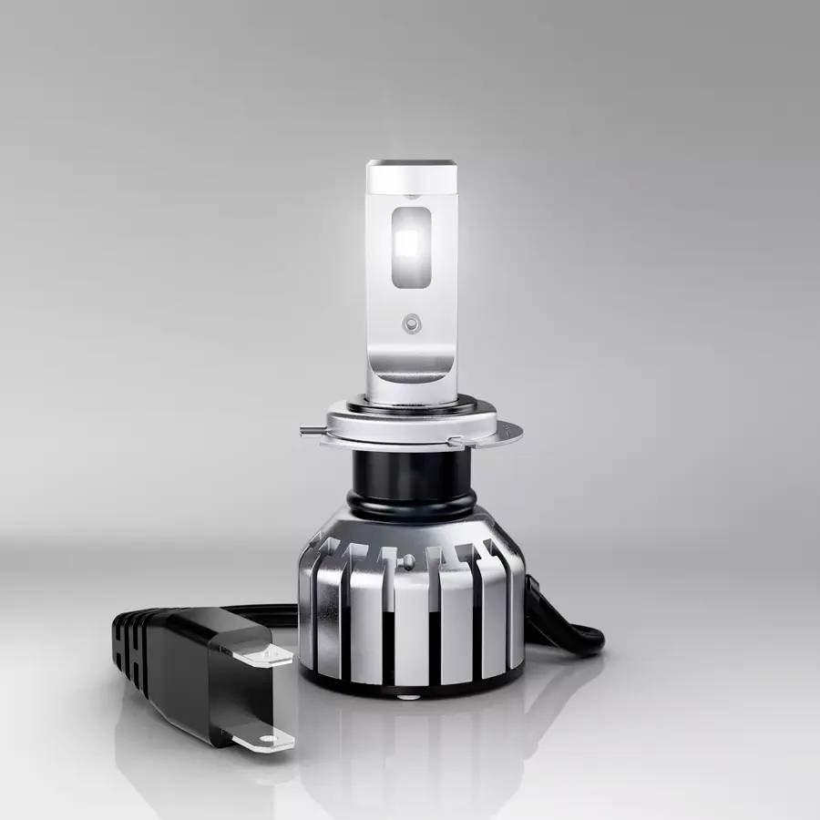 LED-Autolampe mit silbernem Kühlkörper und schwarzem Kabel, auf grauer Oberfläche stehend. Es zeigt eine moderne Beleuchtungstechnologie.