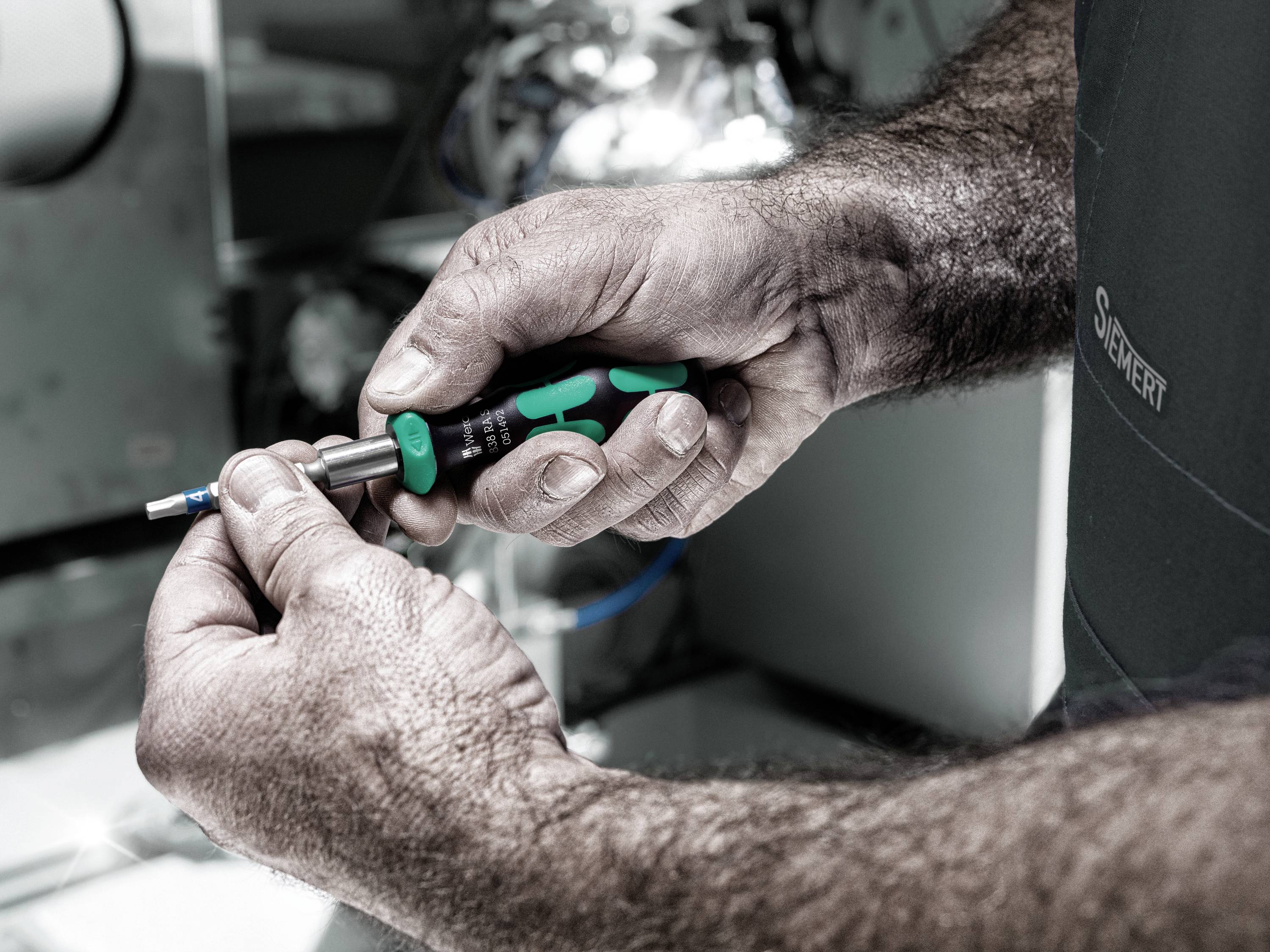 'Nahaufnahme von Händen eines Technikers, der einen Schraubendreher hält und an einer Metallmaschine arbeitet.'