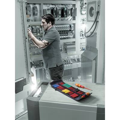 Ein Techniker arbeitet an einem Schaltschrank in einer industriellen Umgebung. Im Vordergrund liegt ein offenes Etui mit Werkzeugen.