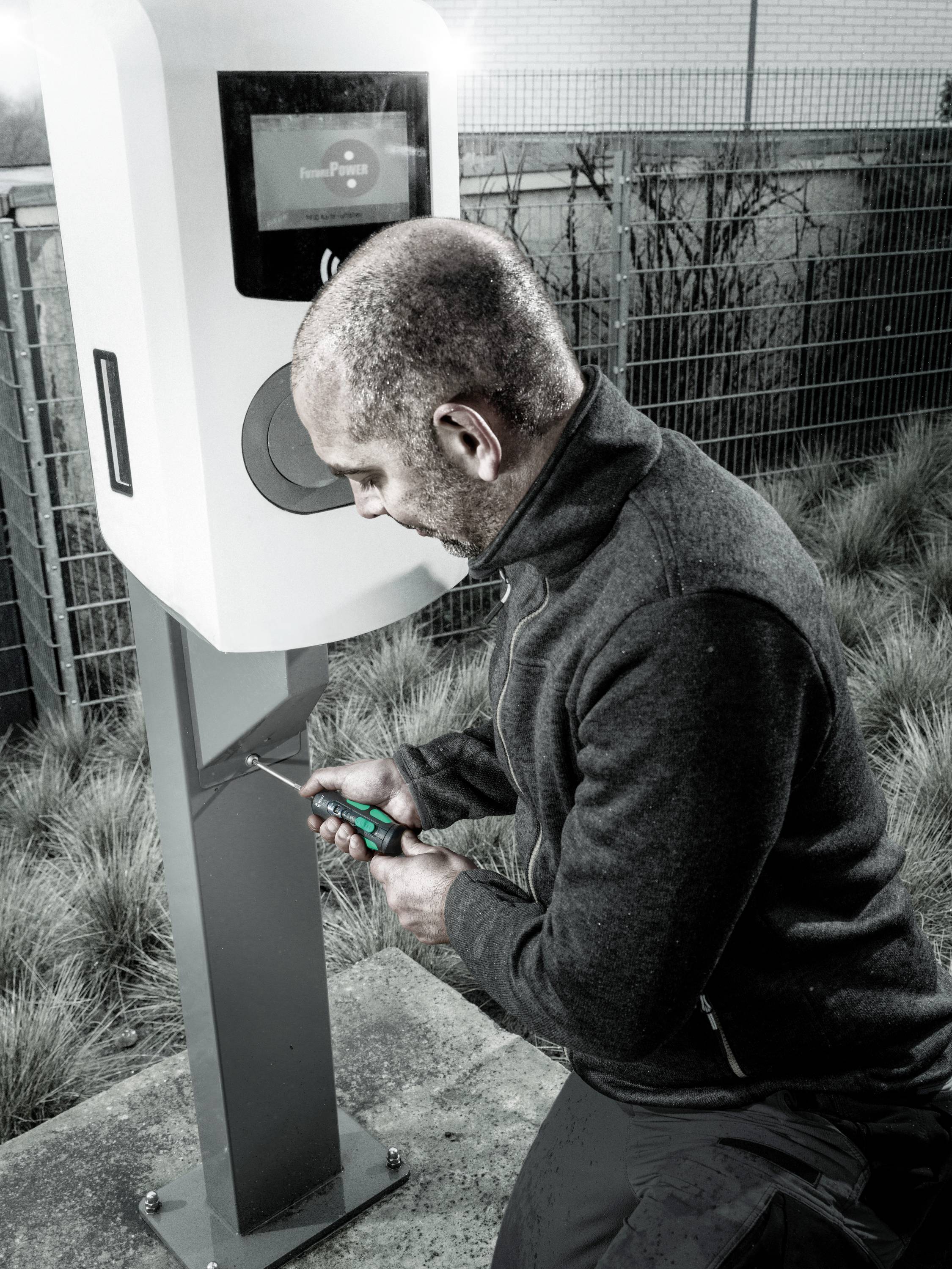 Ein Mann repariert oder installiert eine Ladestation für Elektrofahrzeuge im Freien.