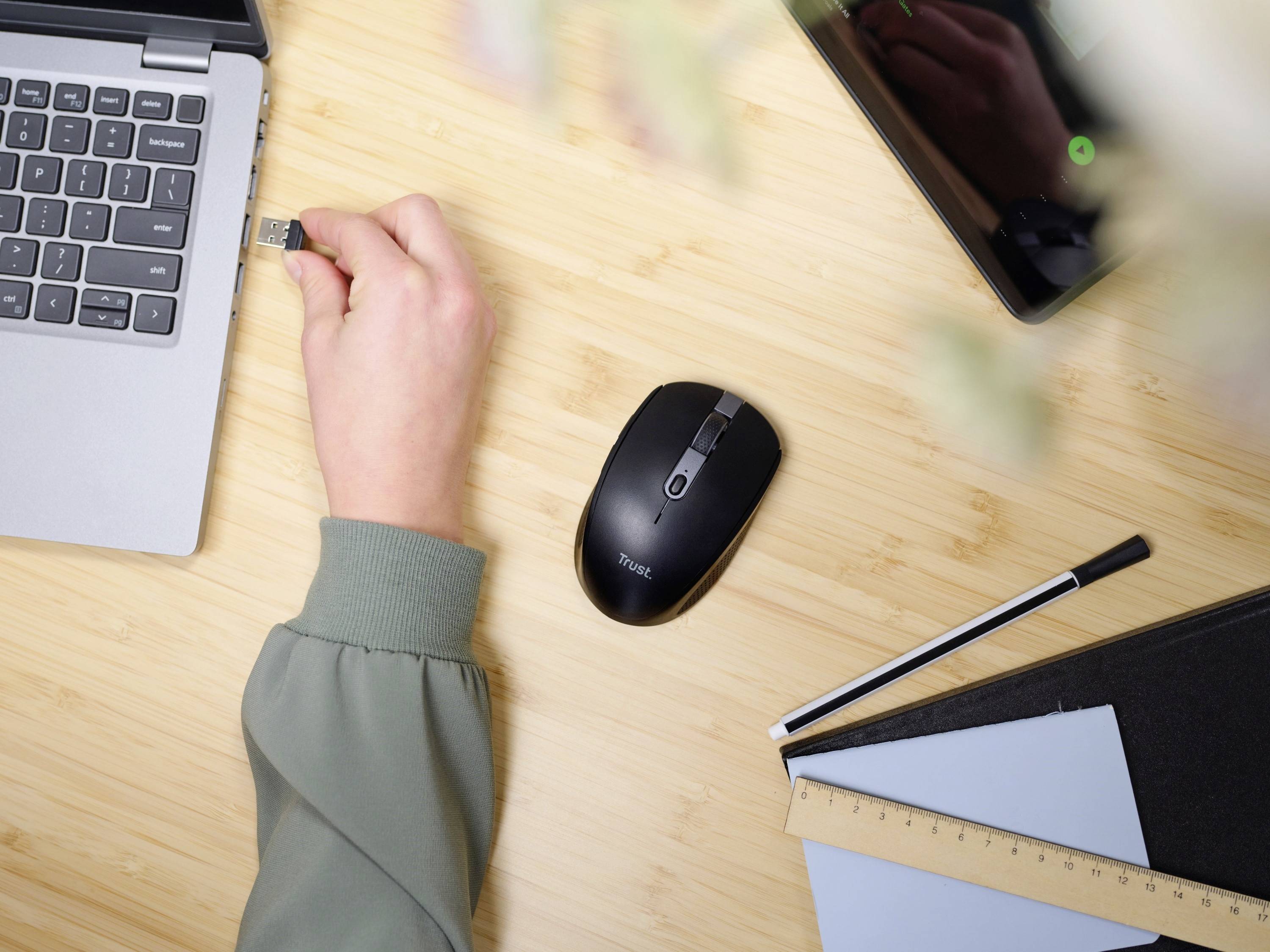 Eine Person steckt einen USB-Stick in einen Laptop auf einem Tisch mit einer kabellosen Maus, einem Tablet, einem Stift und einem Notizbuch.