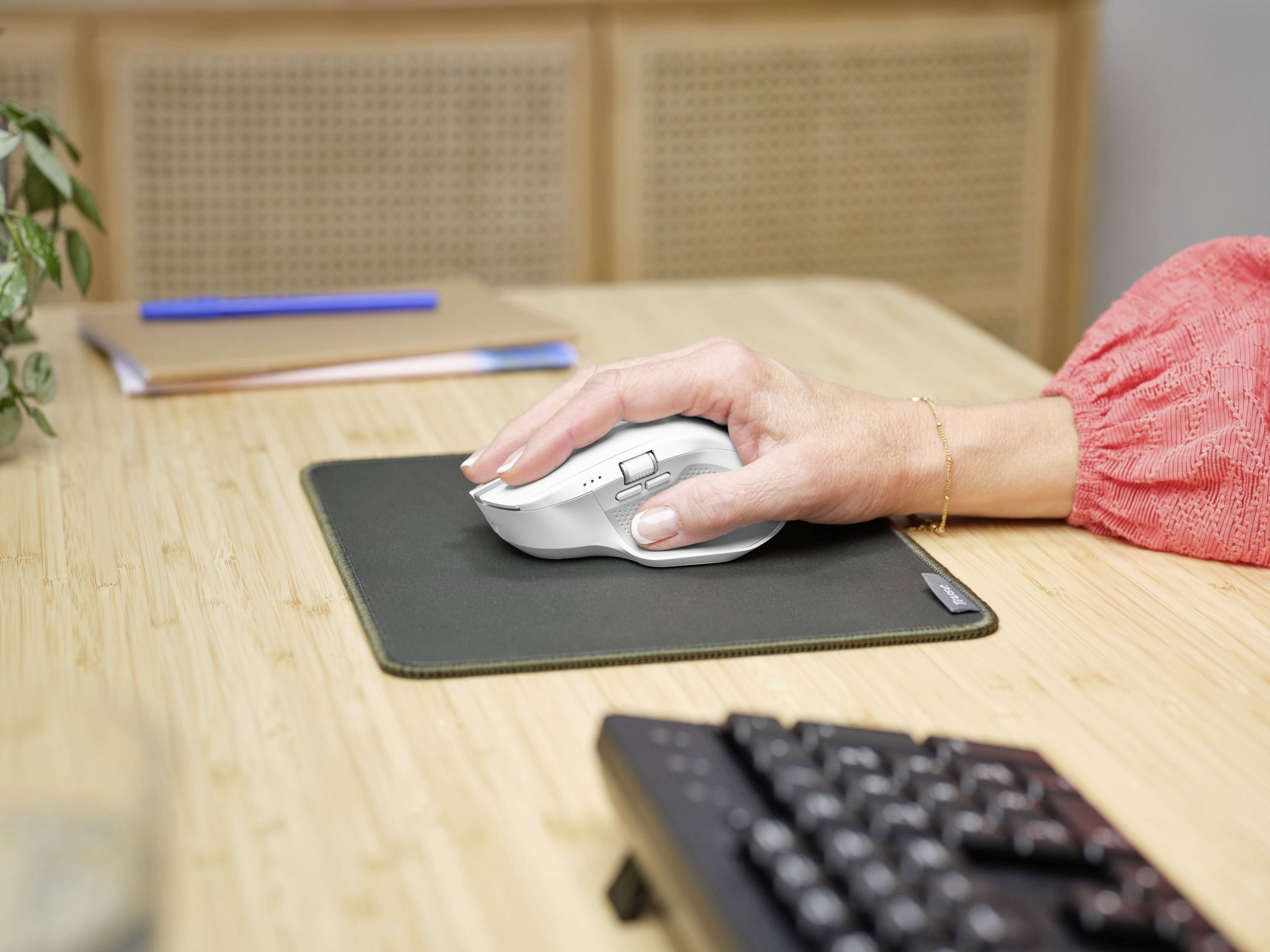 Eine Hand bedient eine weiße Computermaus auf einem dunklen Mauspad auf einem Schreibtisch. Eine Tastatur ist im Vordergrund zu sehen.