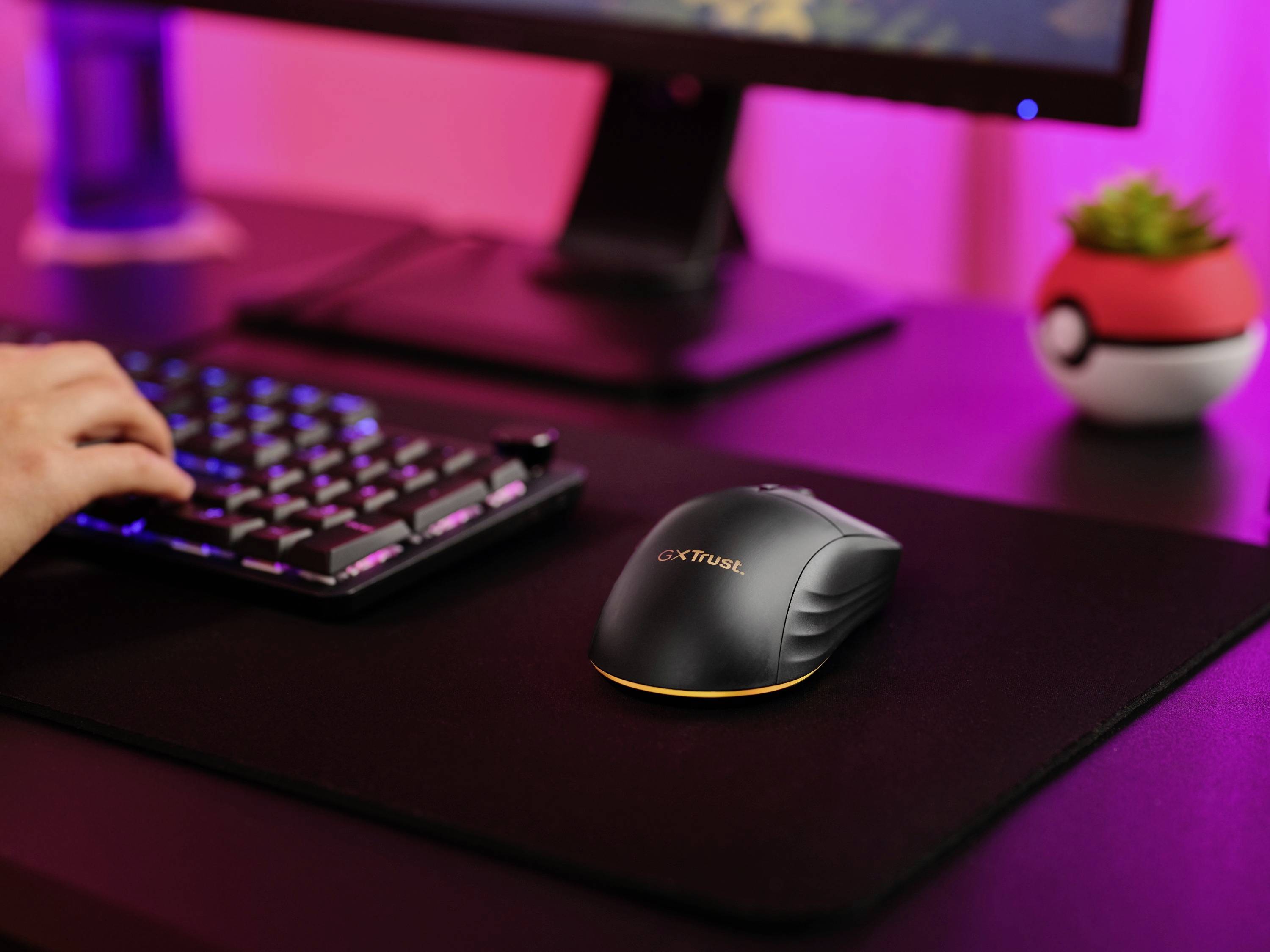 Ein Schreibtisch mit einer Tastatur und einer kabellosen Maus, im Hintergrund ein Bildschirm. Eine Hand tippt auf der Tastatur.