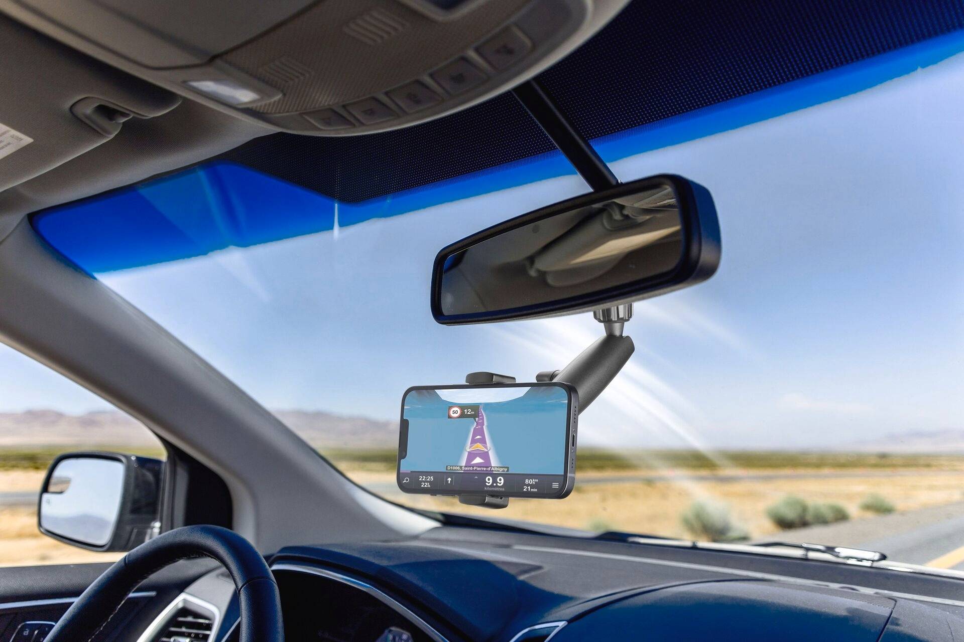 Navigationsgerät im Auto zeigt eine Straße und Landschaft mit Bergen im Hintergrund. Das Gerät zeigt eine Route und verbleibende Kilometer an.