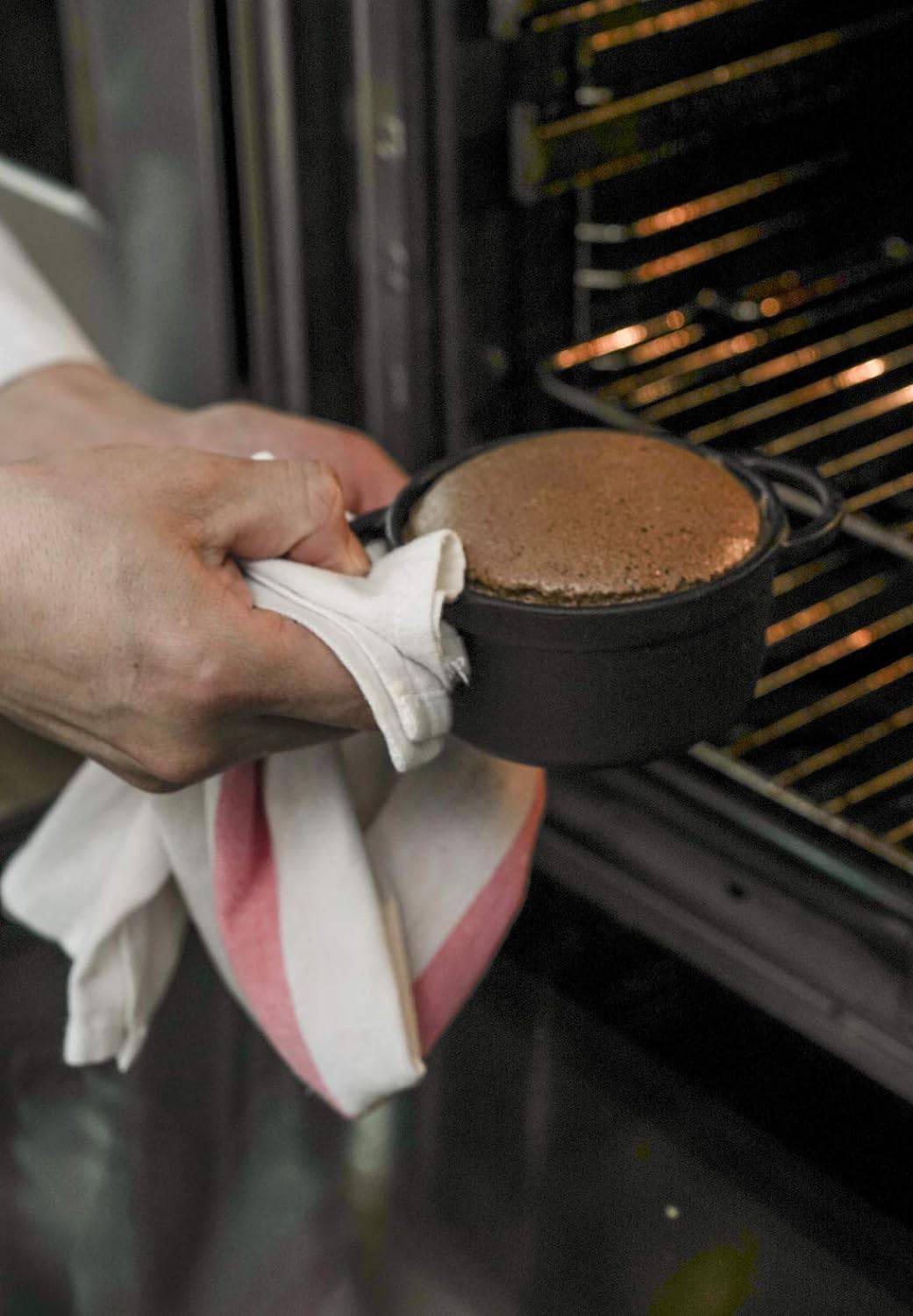 Eine Hand holt ein frisch gebackenes Soufflé aus dem Ofen. Das Soufflé ist aufgegangen und sieht schokoladenbraun aus.