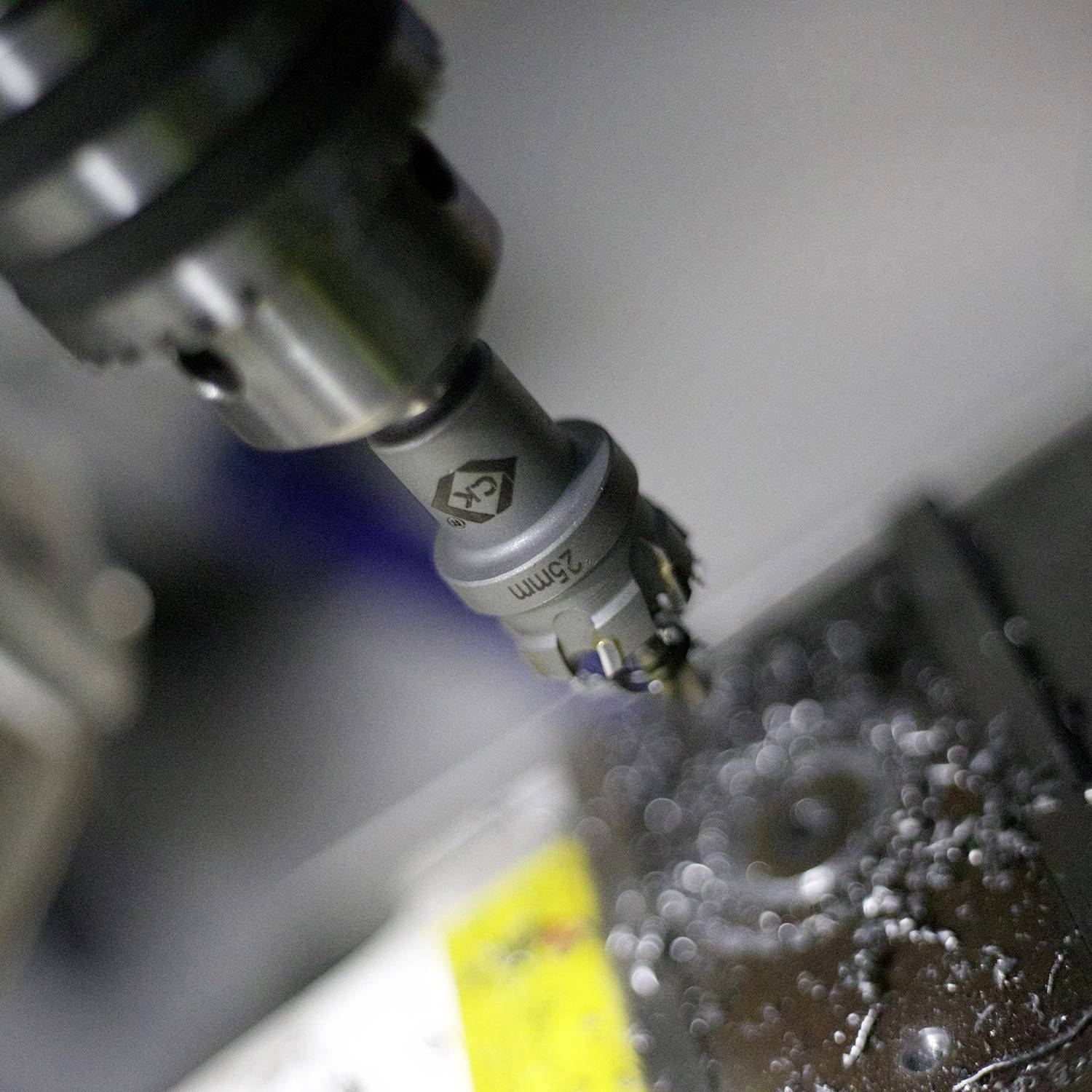 Nahaufnahme eines Bohrers, der ein rundes Loch in eine metallische Oberfläche bohrt. Metallspäne sind um das Bohrloch verteilt.