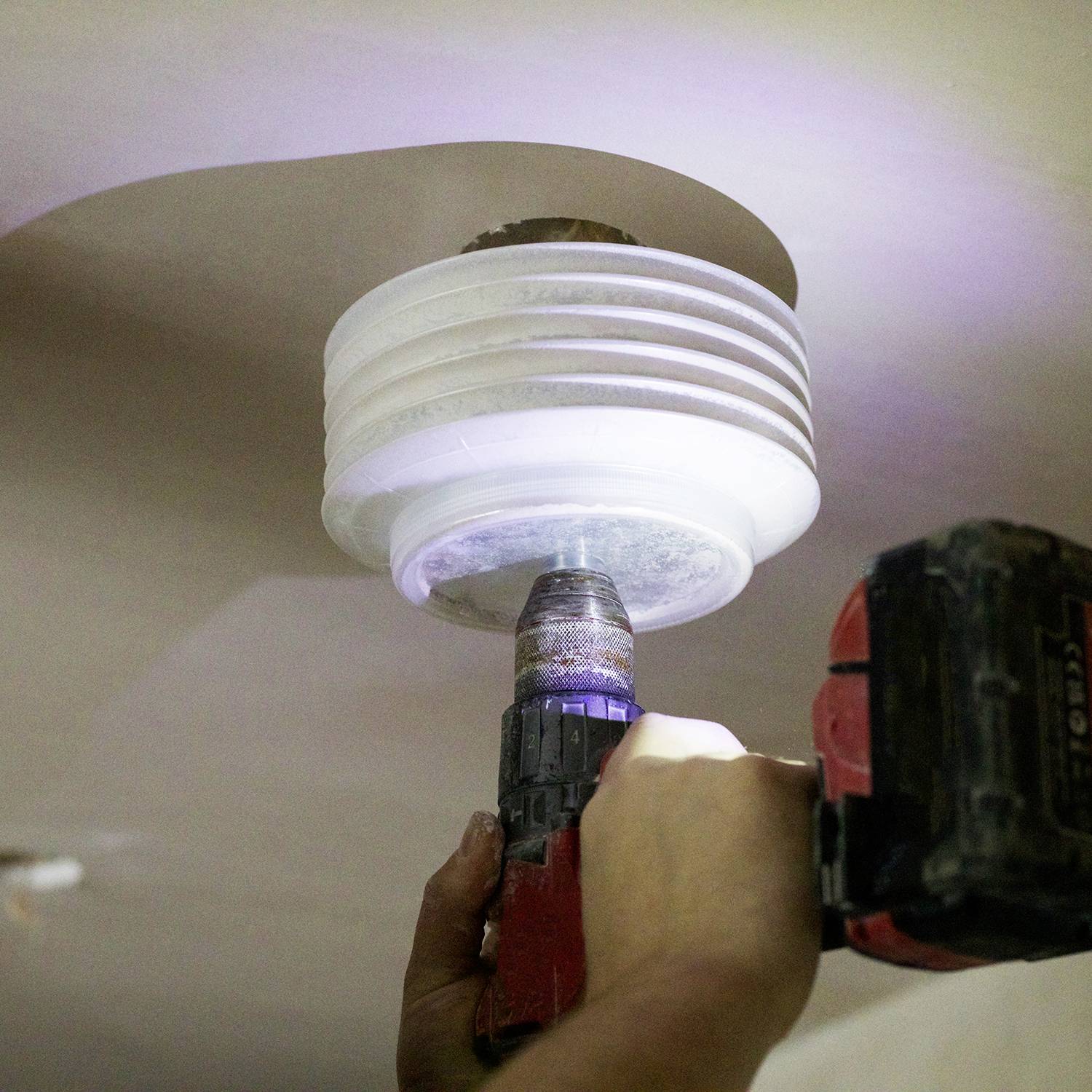 Eine Person repariert eine Deckenlampe mit einem Akkuschrauber. Die Hand hält das Werkzeug, das eine weiße runde Abdeckung befestigt.